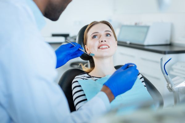a woman sitting in a dental chair looking at the dentist who is holding dental tools, depicting a dental checkup